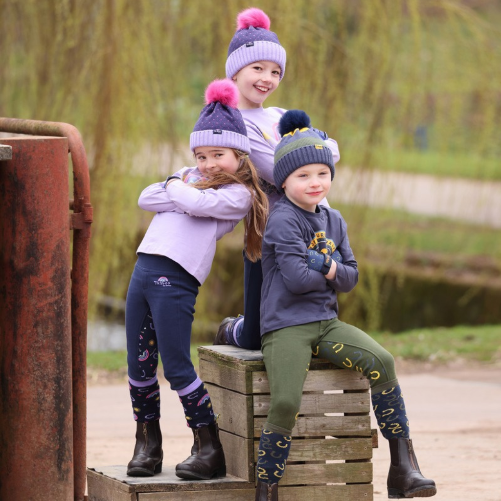 Three young riders in bobble hats and jodhpurs sitting on a wooden crate in the yard