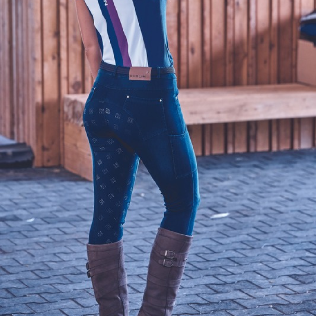 Woman in navy Dublin jodhpurs and tall boots by a timber fence
